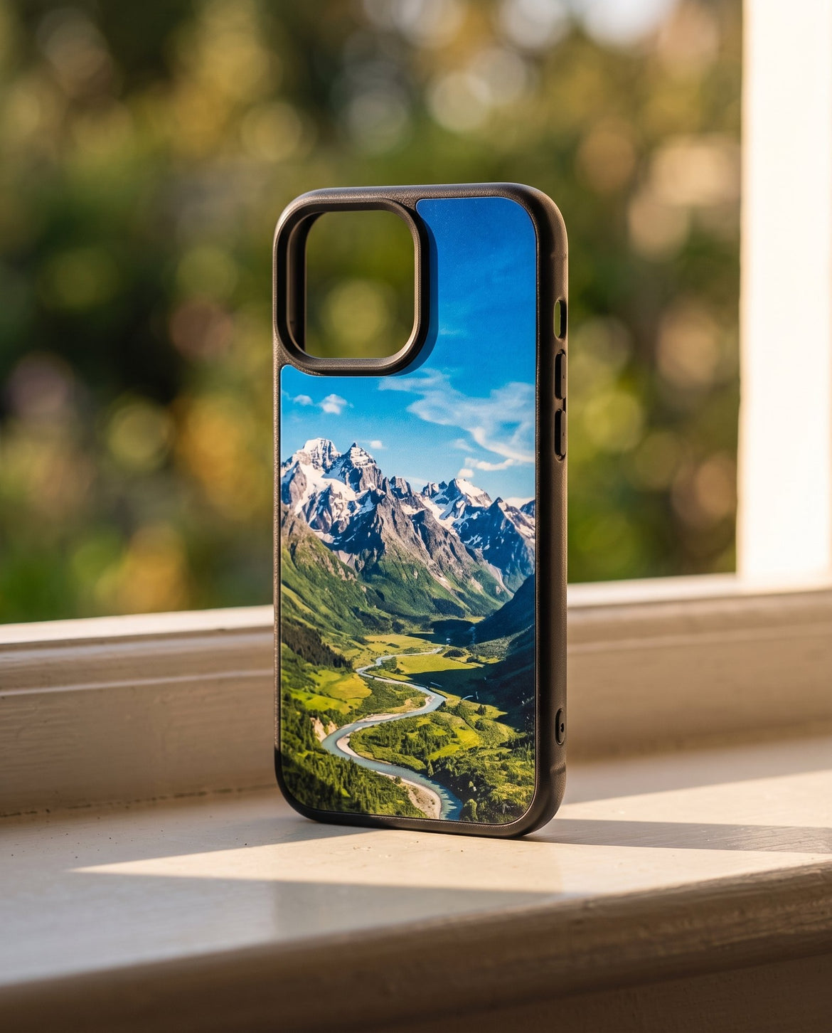 A Kase Artist case standing on a sunlit windowsill in late afternoon light, printed with a photograph of a mountain valley, a garden blurred behind it