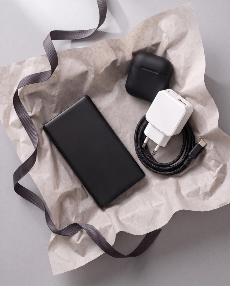 The Kase Artist gift set laid in tissue paper with a ribbon, showing the power bank, wall charger, braided cable and wireless earbuds